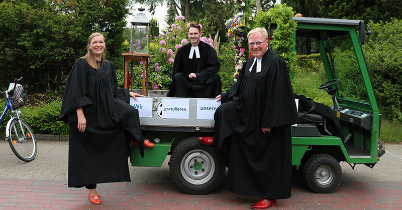 Pastorin Laura Koch-Pauka, Vikar Alexander Bieniasz und Pastor Harald Schmidt sitzen auf einem kleinen Trekker, dem Konfi-Mobil.