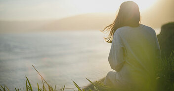 Frau auf einer Klippe blickt in Sonnenaufgang - Copyright: Unsplash, Artem Kovalev