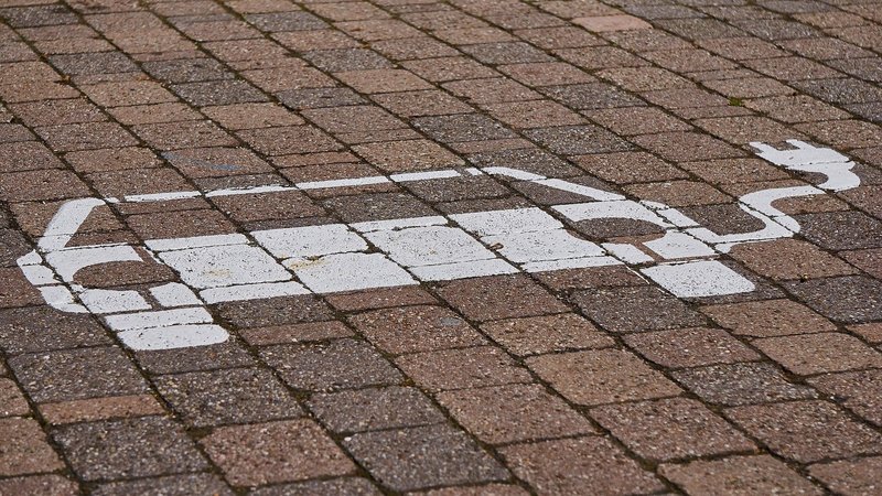 Ein weißes E-Fahrzeug als Symbol eines PKW mit Stecker und Kabel auf einem gepflasterten Parkplatz.