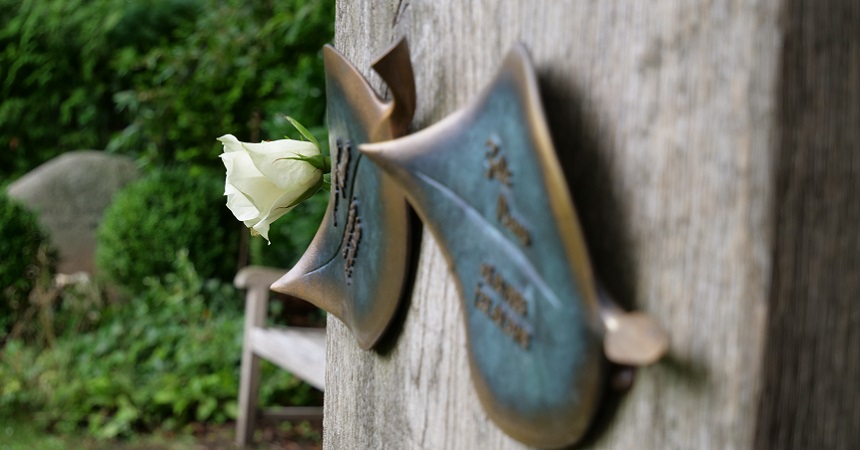 Die Kupferblätter an der Holzstele tragen die Namen Verstorbener. Die Urnen sind um die Stele herum zur Ruhe gebettet. Der Bereich wird von den Friedhofsgärtnern gepflegt.